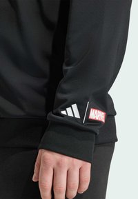 Czarna sportowa bluza z długimi rękawami. Na lewej rękawie znajduje się biały logo Adidas oraz czerwony logo Marvel. Gładka, elastyczna tkanina.