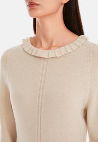 Beige Pullover mit geripptem Kragen und subtiler Textur. Hat ein tailliertes Design und vertikale Nahtdetails, gefertigt aus weichem Strickmaterial.