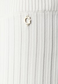 Tecido tricotat cu nervuri de culoare gri deschis prezintă un accent mic cu logo-ul auriu "G" pe lateral, adăugând un detaliu subtil designului.