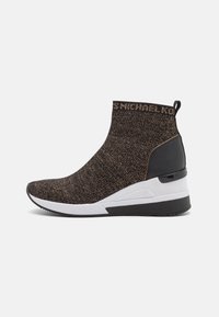 Baskets montantes tricotées en noir et or avec une semelle blanche et noire épaisse. Présente un logo au niveau de la cheville et un accent noir lisse au niveau du talon.