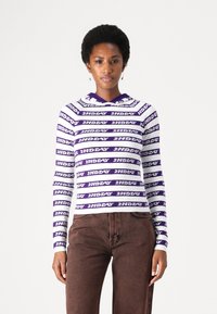 Maglietta bianca a maniche lunghe con strisce orizzontali viola che presenta il testo "2NDAY". Il tessuto appare liscio, con un design aderente e cappuccio.
