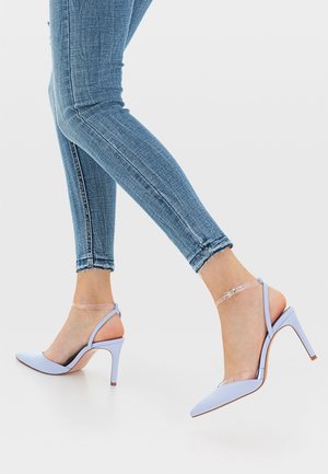 Chaussures à talons hauts bleu clair, avec un bout pointu, des brides de cheville transparentes et une finition lisse et brillante. Portées avec un jean slim bleu.