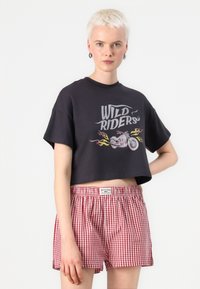 Black cropped t-shirt with "WILD RIDERS" graphic and motorcycle print; paired with red and white checked shorts.