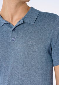Polo de hombre de manga corta en azul jaspeado, tejido de punto, con cuello plano, tapeta de dos botones y un logo sutil en el pecho.