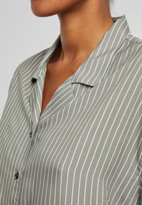 Light green shirt featuring vertical white stripes, a notched collar, and black buttons on the front, with a smooth texture.