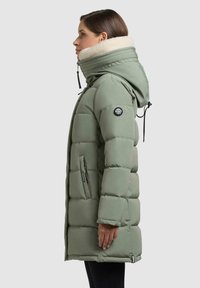 Padded green parka z wysokim kołnierzem, ocieplonym wnętrzem, regulowanym kapturem, bocznymi kieszeniami i okrągłą łatą z logo na rękawie.