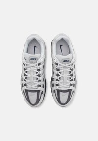Nike sportcipő, amely szürke és fehér hálós és szintetikus felsőrészből készült, sötétszürke részletekkel, valamint textúrált talppal a tapadás érdekében.