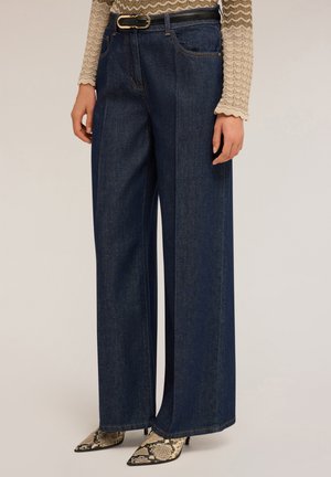 Wijde donkerblauwe denim broeken met een hoge taille, voorzien van steekzakken en een strakke zwarte riem. Geverfde slangenhuid hakken.