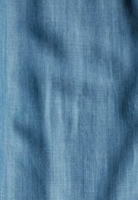 Denimtyg i ljusblått med en slät textur och subtila vertikala linjer, som visar på lätta rynkor för ett avslappnat utseende.