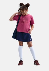 Camiseta de algodón rosa con el texto "ES HORA DE BRILLAR", falda marina, calcetas blancas hasta la rodilla y zapatillas burdeos. Incluye un bolso oscuro de hombro.