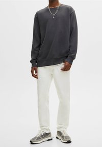 Sudadera gris oscura con cuello redondo, mangas largas y puños acanalados, combinada con jeans blancos de corte ajustado y zapatillas grises.
