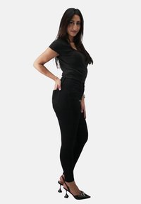 Czarne dopasowane dżinsy z wysokim stanem i tylnymi kieszeniami. Połączone z czarną bluzką i czarnymi butami na obcasie z dekoracyjnym akcentem.