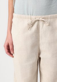Pantaloni elasticizzati beige chiaro con regolazione in vita, realizzati in un tessuto testurizzato, dotati di tasche laterali e dalla vestibilità comoda.