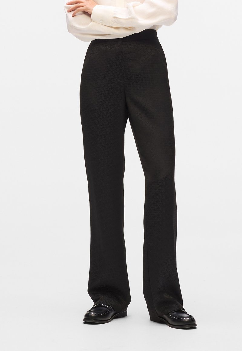Pantaloni neri con un motivo testurizzato, caratterizzati da un design a gamba dritta e un'alta vita. Abbinati a scarpe nere e una blusa leggera.