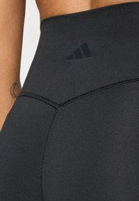 Czarne legginsy sportowe o wysokim stanie, z gładką teksturą, z tonalnymi szwami i małym czarnym logo adidas na pasku.