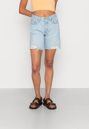 Light blue denim shorts with distressed detailing, frayed hem, and a mid-rise fit, paired with dark brown sandals featuring buckles.