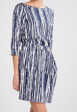 Woman wearing a knee-length dress with navy and white vertical brushstroke stripes and three-quarter sleeves, standing against a plain background.