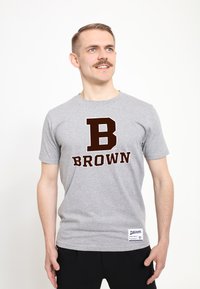 Grå t-shirt med korte ærmer, der har et stort mørkebrunt "BROWN" print og et fremtrædende "B" logo på forsiden. Tekstil i struktureret bomulds materiale.