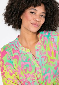Camicia a bottoni colorata con stampa animale verde, rosa e blu. Presenta un colletto e una vestibilità morbida con una texture soffice.