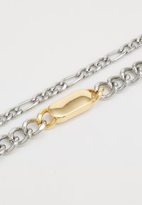 Zilveren en gouden schakels met afwisselende metaalafwerkingen; bevat een gladde, langwerpige gouden schakel als een centraal punt.