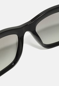 Schwarze Sonnenbrille mit glatter Oberfläche, grauen Verlaufsgläsern, dicken Fassungen und abgerundeten Kanten. Keine sichtbaren Logos oder Muster.