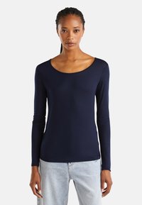 Granatowa bluzka z długim rękawem, wykonana z gładkiego materiału z szerokim dekoltem w serek, dopasowanym krojem i subtelnymi detalami przeszycia. Połączona z jasnymi dżinsami.