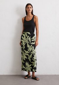 Čierny rebrovaný top s ramienkami v kombinácii s dlhou vzorovanou sukňou s veľkými zelenými kvetinovými motívmi. Model má na nohách tmavé ploché sandále.