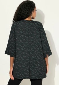 Tunic nera con motivo floreale in teal e grigio, maniche a tre quarti e spacchi laterali, realizzata in tessuto strutturato. Presenta un design dritto sul retro.