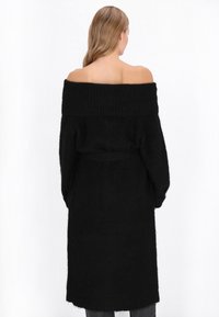 Cardigan tricotat negru, cu umerii goi, cu o croială lejeră, mâneci lungi și un model texturat cu rigle. Dispune de un cordon în talie și un tiv până la genunchi.