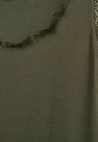 Olíva zöld, bordázott felső, csipkés, fodros díszítéssel a nyakvonal mentén. Puha anyag, testhezálló fazon.