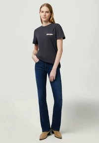 Grå bomulds t-shirt med rund hals og korte ærmer, parret med mørkeblå flagrende jeans og beige hælbukser.