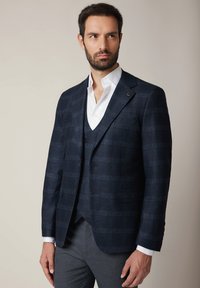 Granatowa marynarka w kratę z teksturowanej tkaniny o dopasowanym kroju, z jednoprzodowym zapięciem i szpiczastymi klapami, w połączeniu z białą koszulą.