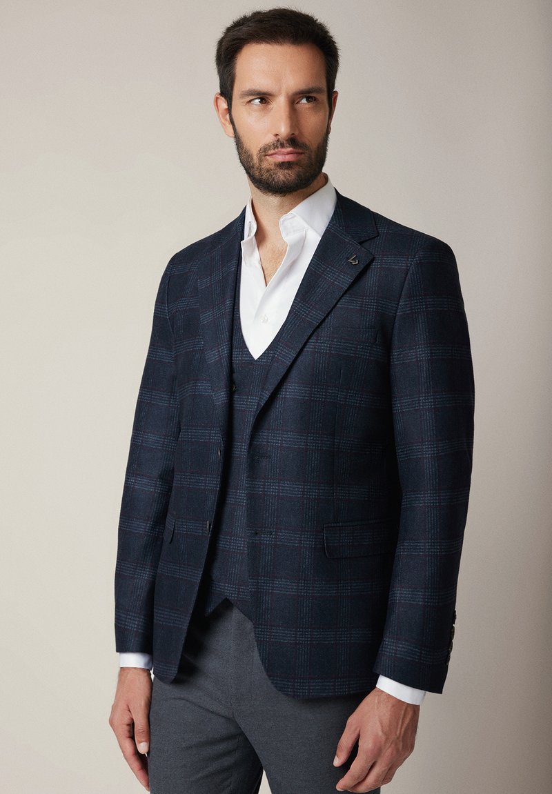 Granatowa marynarka w kratę z teksturowanej tkaniny o dopasowanym kroju, z jednoprzodowym zapięciem i szpiczastymi klapami, w połączeniu z białą koszulą.
