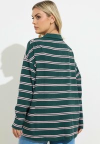 Zielona i różowa w paski koszula z długimi rękawami i kołnierzykiem, cechująca się teksturowanym materiałem i luźnym krojem. Widok z tyłu.