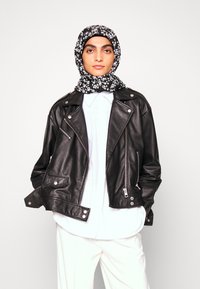 Casaco de couro preto estilo biker com fechos e botões prateados, combinado com uma blusa branca e um lenço com padrão floral em preto e branco.