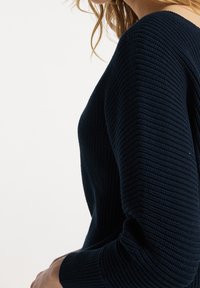 Granatowy sweter z prążkowanego dzianego materiału z długimi rękawami, dopasowany fason i fakturowana tkanina. Charakteryzuje się szerokim dekoltem i subtelną elastycznością dla komfortu.