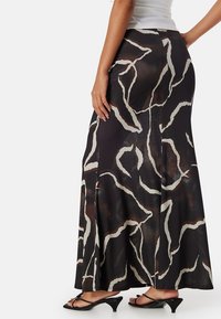 Maxi rok in het zwart met een vloeiende silhoutte, voorzien van een wit abstract patroon en een soepele textuur. Dit ontwerp heeft zijsplitten voor extra beweeglijkheid.