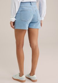Pantalones cortos de mezclilla azul claro con cintura alta, que cuentan con dos bolsillos traseros y un dobladillo sin rematar. Combinados con zapatillas verde claro.