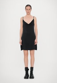Rochie neagră cu guler în formă de cowl, cu bretele subțiri, textură netedă și tăieturi laterale. Asortată cu bocanci negri cu șireturi și curele pentru gleznă.