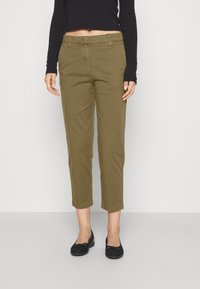 Olivgröna kortbyxor med en åtsittande midja och raka ben, kombinerat med svarta platta skor. Tyget ser slätt ut och har framfickor.