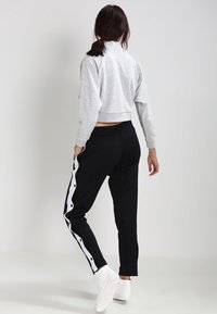 Kortgrijze sweatshirt met lange mouwen, gecombineerd met zwarte broek met witte zijknoppen en een gladde textuur, geschikt voor sportkleding.