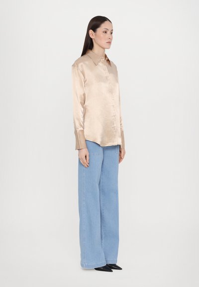 Satin beige long-sleeve shirt with button closure and contrasting collar, paired with light blue wide-leg jeans and black pointed shoes.