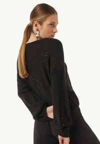 Schwarzer Strickpullover mit lockerer Passform, der dezente glitzernde Details und einen weiten Ausschnitt aufweist. Lange Ärmel mit gerippten Abschlüssen.