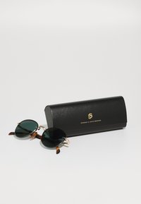 Ochelari de soare rotunzi, de culoare verde închis, cu accente din metal auriu. Temele cu imprimeu țestoasă. Etui negru din piele cu logo embosat, design compact.