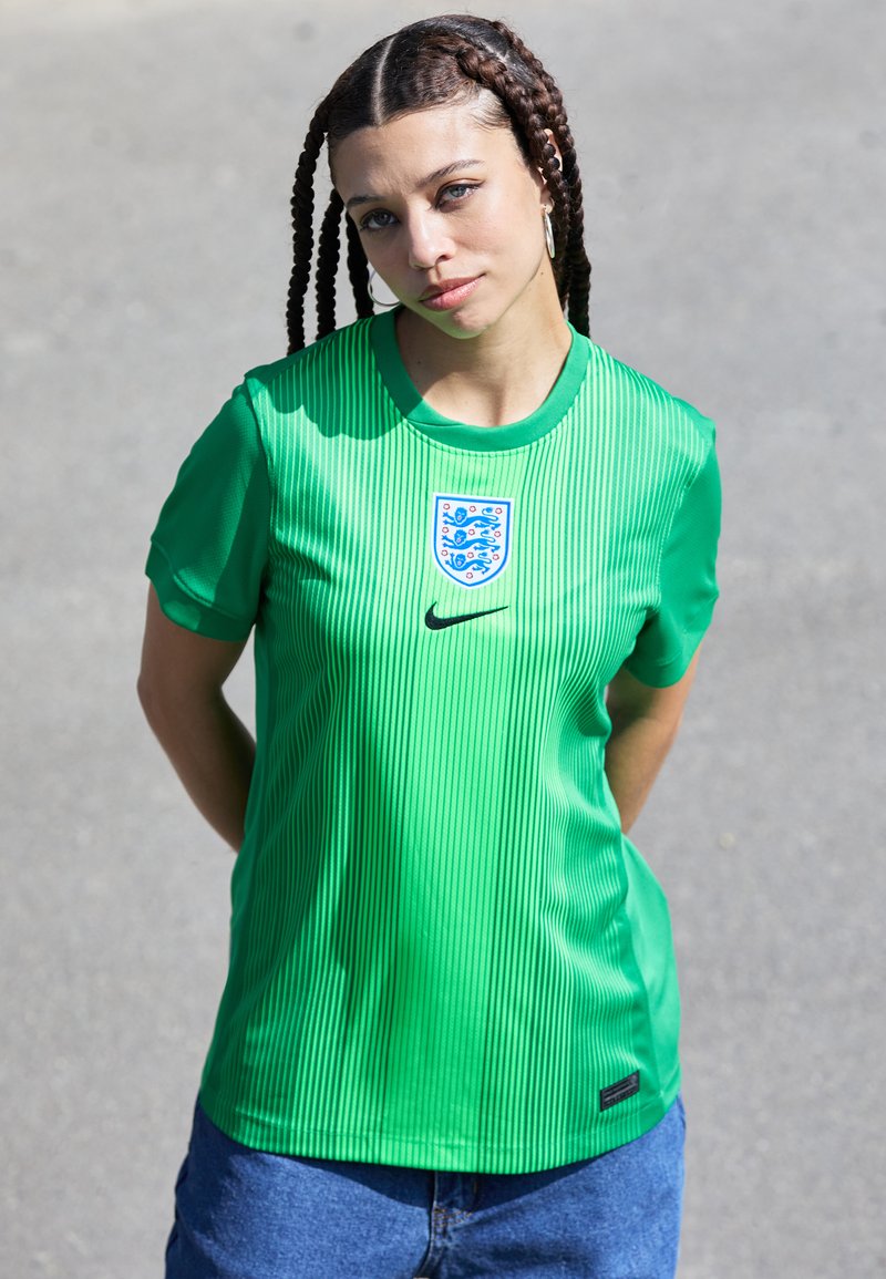 Zaļš sporta krekls ar vertikālām svītrām, apaļu kakla izgriezumu un Anglijas futbola emblēmu. Izcelts Nike logo. Gluda tekstūra.