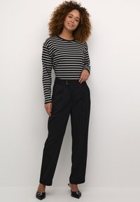 Chemise rayée noir et blanc à manches longues associée à un pantalon noir taille haute avec une fermeture à boutons à l'avant et des jambes fuselées.
