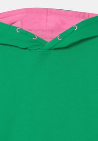 Sudadera verde con interior forrado en rosa y ojales a juego en rosa en los agujeros del cordón.