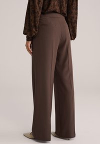 Pruunid, kohandatud laiade säärtega püksid, mis on sileda tekstuuriga ja millel on varjatud tagataskud, kombineeritud tekstuurse tumepruuni topiga.