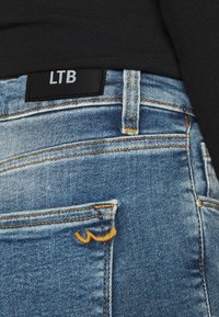 Ljust blå denimjeans med en svart LTB-etikett, med gula stygn, en blek textur och bakfickor med dekorativa stygn.