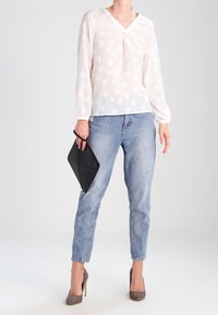 Blusa bianca a maniche lunghe con motivo a stelle e scollatura a V, abbinata a jeans azzurri e una clutch nera. Tacchi alti grigi completano l'outfit.